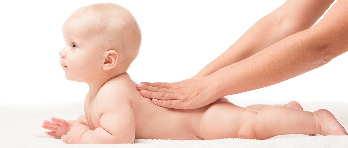 Cute baby lying on white blanket on stomach hands massaging his back. Isolated over white background.